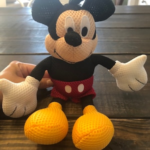 May include: A black and yellow mesh Mickey Mouse plush toy. The toy has a red and white polka dot shorts and a big smile.
