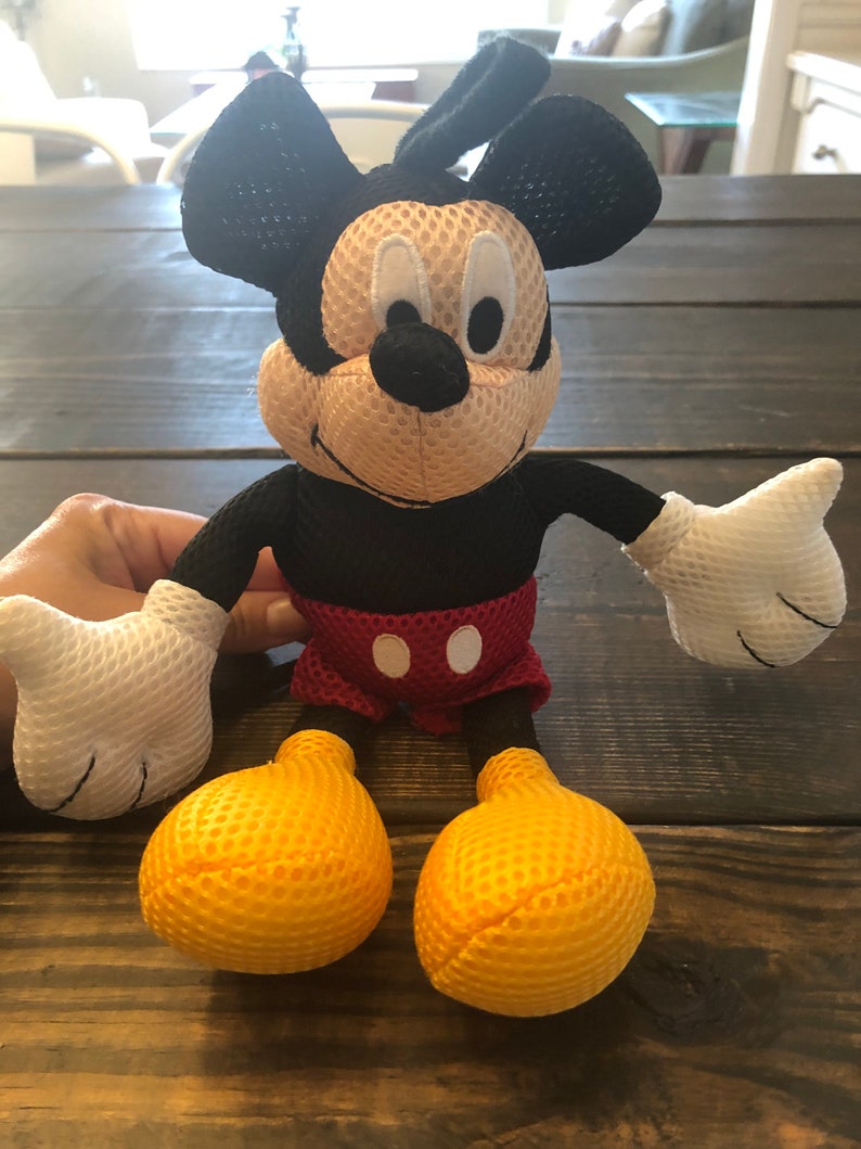 May include: A black and yellow mesh Mickey Mouse plush toy. The toy has a red and white polka dot shorts and a big smile.