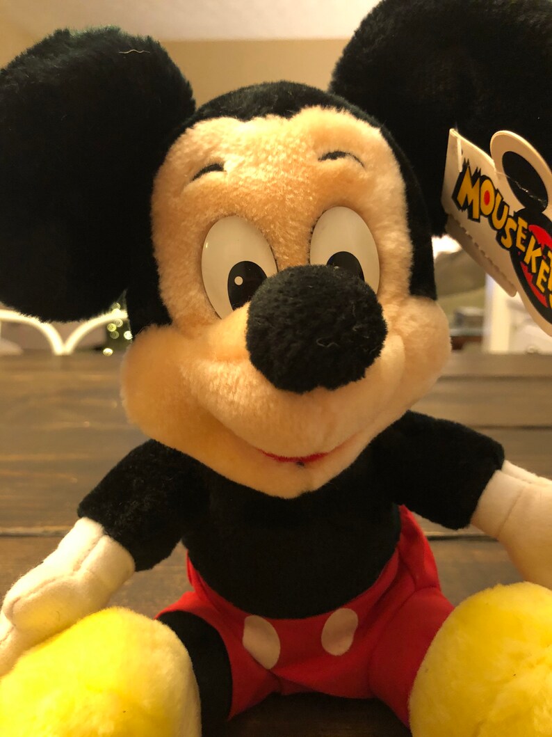 May include: A plush Mickey Mouse toy with black fur, large white eyes, and a red and white polka dot shorts. The toy has a yellow tag that says "Mouseketeers".