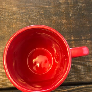 May include: A red ceramic mug with a smooth, glossy finish. The mug is empty and has a handle.