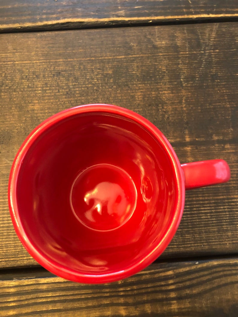 May include: A red ceramic mug with a smooth, glossy finish. The mug is empty and has a handle.