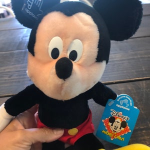 May include: A plush Mickey Mouse toy wearing red shorts with yellow buttons. The toy has a blue tag that says "Disney's Mickey & Pals" with a picture of Mickey Mouse on it.