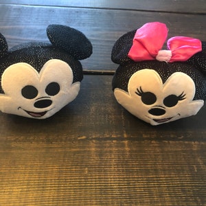 May include: Two plush toys of Mickey Mouse and Minnie Mouse. Mickey Mouse is black with white accents and Minnie Mouse is black with white accents and a pink bow.