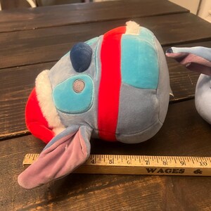 May include: A plush toy in the shape of a cartoon character's head, featuring blue, red, and white colors. The toy has large ears and a round head. A wooden ruler is placed next to the toy.