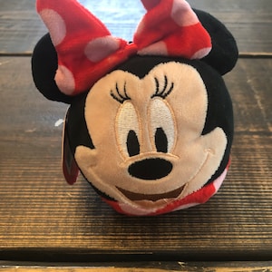 Op de afbeelding: Een pluche speelgoed van Minnie Mouse met een rode strik met witte stippen. Het speelgoed is zwart, bruin en rood.