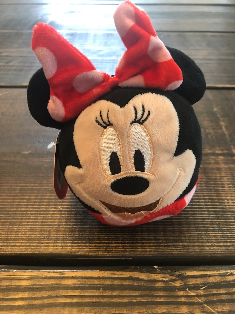 Op de afbeelding: Een pluche speelgoed van Minnie Mouse met een rode strik met witte stippen. Het speelgoed is zwart, bruin en rood.