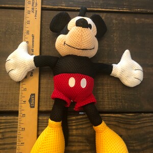 May include: A black and red Mickey Mouse plush toy with yellow mesh shoes. The toy is made of a soft, mesh material and has a friendly expression.