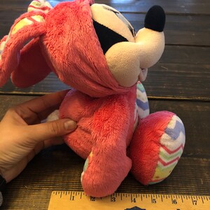 Op de afbeelding: Roze pluche konijn met een kleurrijk paasei-patroon. Het konijn heeft een zwarte neus en grote oren.