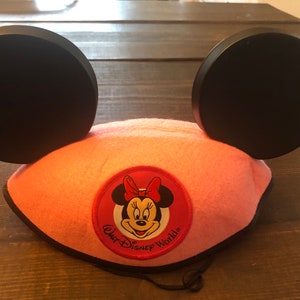 May include: Pink Minnie Mouse ears headband with black ears and a red and white Minnie Mouse face patch that says "Walt Disney World".