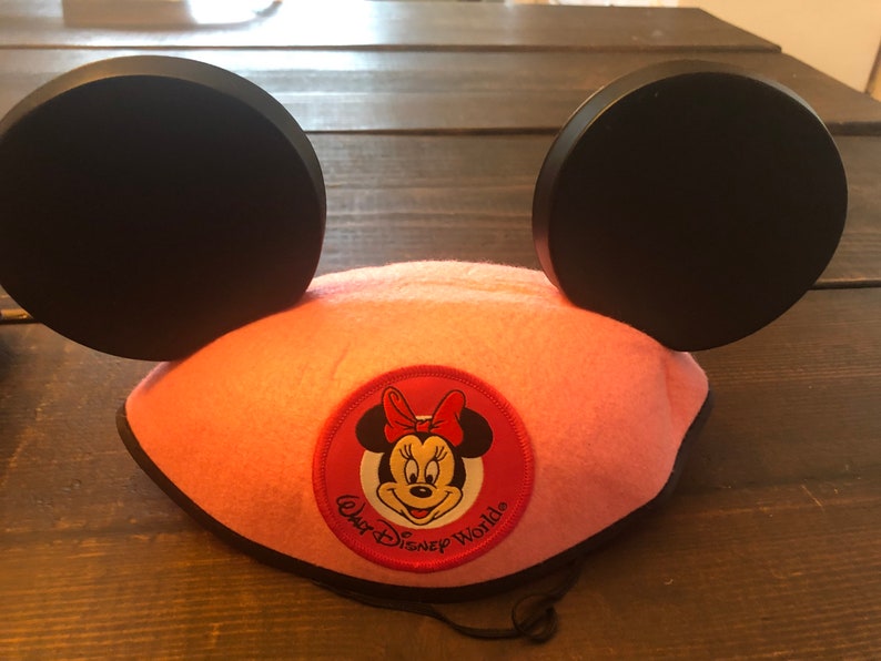 May include: Pink Minnie Mouse ears headband with black ears and a red and white Minnie Mouse face patch that says "Walt Disney World".