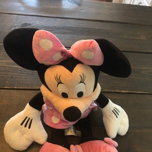 May include: A plush Minnie Mouse toy with pink polka dot bow and dress. The toy has black ears, a black nose, and white eyes.