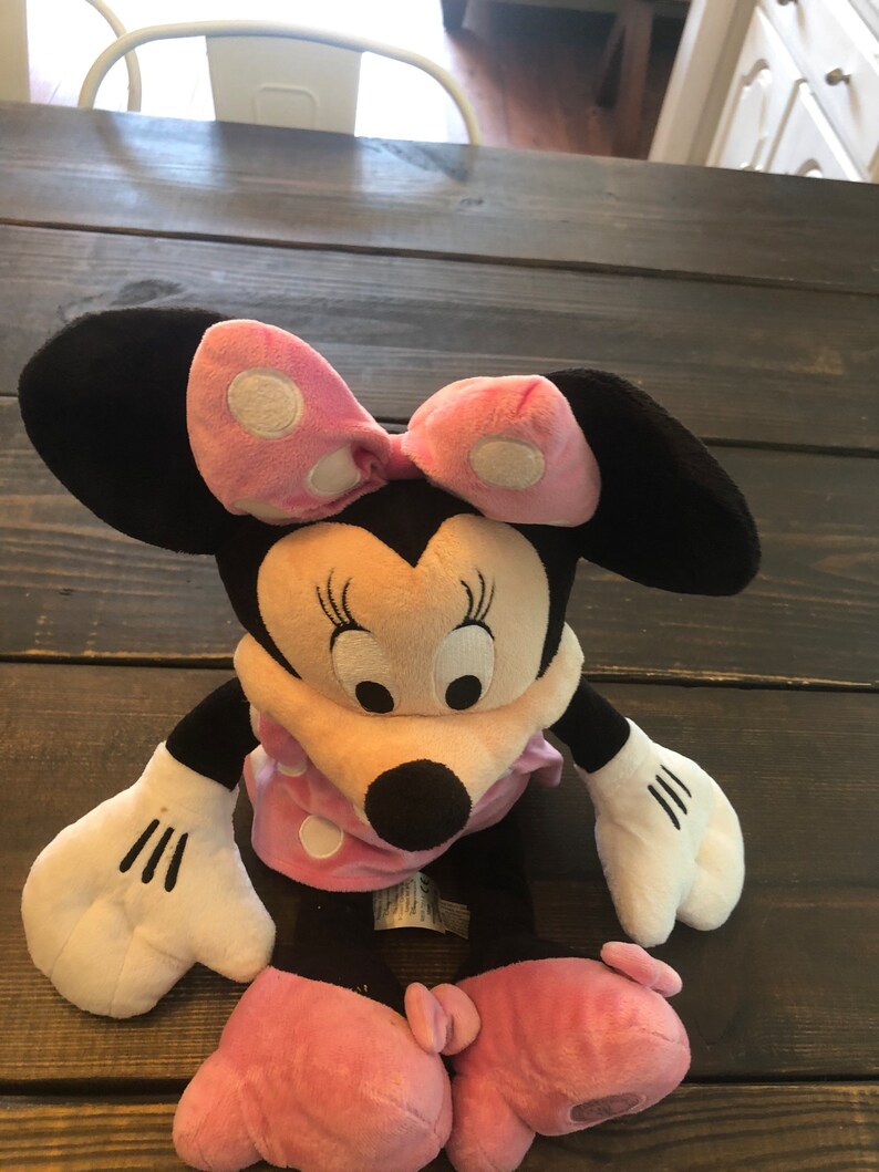 May include: A plush Minnie Mouse toy with pink polka dot bow and dress. The toy has black ears, a black nose, and white eyes.
