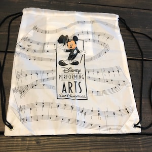 May include: White drawstring bag with a black and white design featuring Mickey Mouse in a conductor's outfit. The bag has the text "Disney Performing Arts" and "Walt Disney World."
