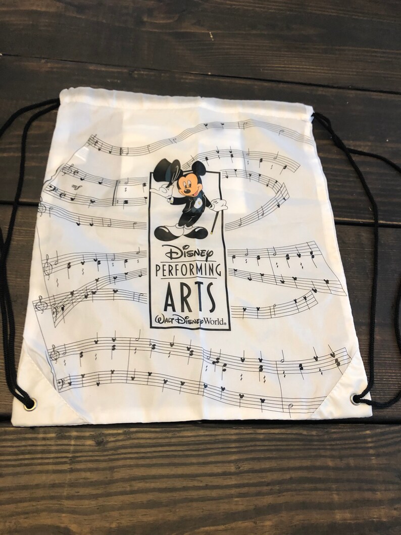 May include: White drawstring bag with a black and white design featuring Mickey Mouse in a conductor's outfit. The bag has the text "Disney Performing Arts" and "Walt Disney World."