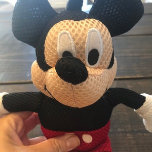 May include: A black and red plush Mickey Mouse toy with a mesh fabric covering. The toy has large black ears, a black nose, and white eyes.