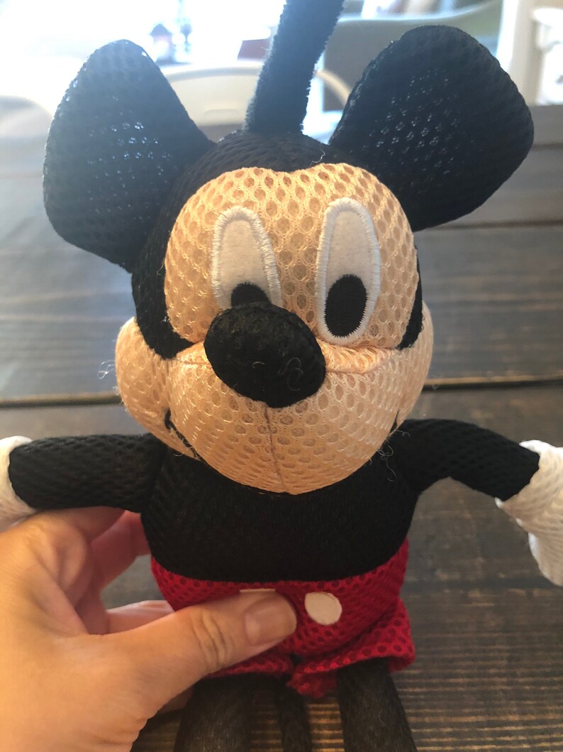 May include: A black and red plush Mickey Mouse toy with a mesh fabric covering. The toy has large black ears, a black nose, and white eyes.
