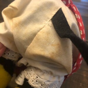 May include: A plush bee toy with yellow and black stripes, wearing a white dress with red polka dots and a black bow. The dress has a white lace trim and the bee has a black and white striped tail.
