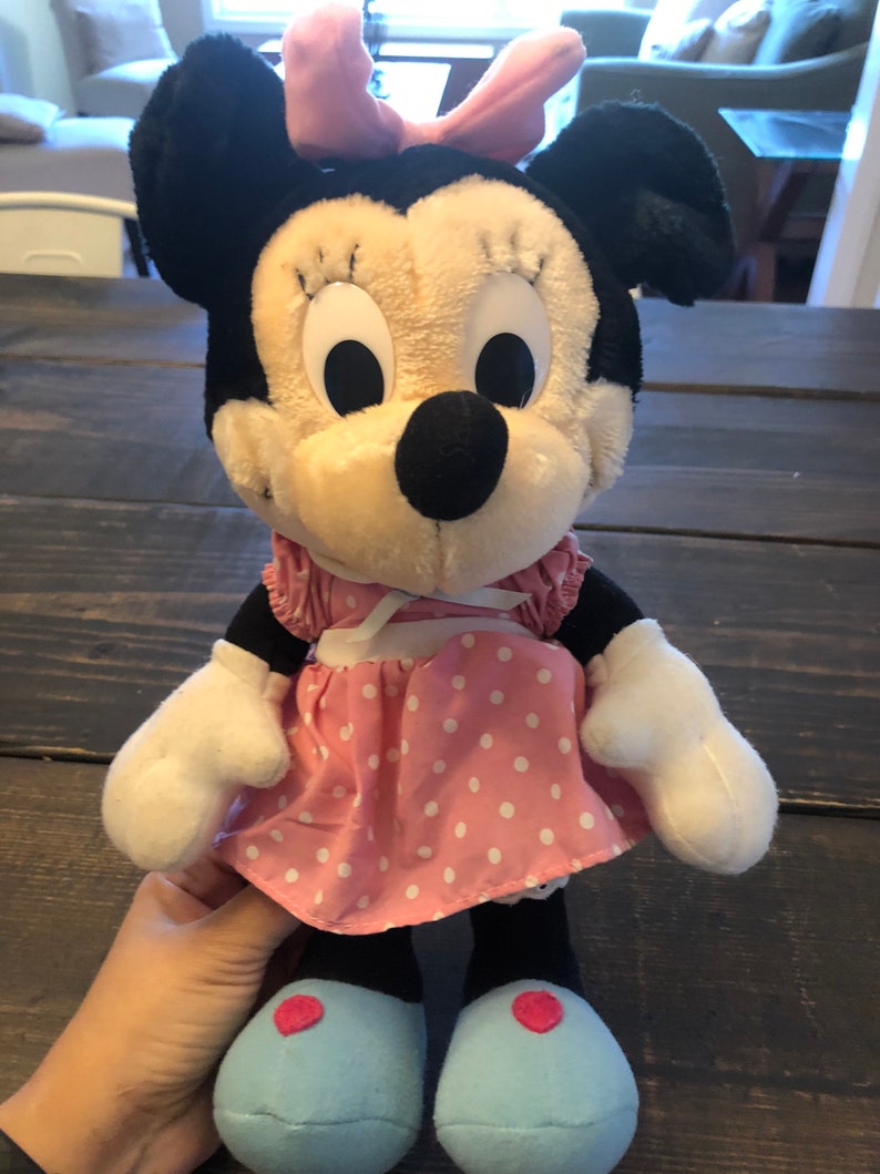 May include: A plush toy of Minnie Mouse wearing a pink polka dot dress with a white bow. She has black ears, a black nose, and large white eyes.