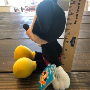 May include: A black and red plush Mickey Mouse toy with yellow shoes and a white tag that says "Disney's Mickey Mouse Clubhouse".
