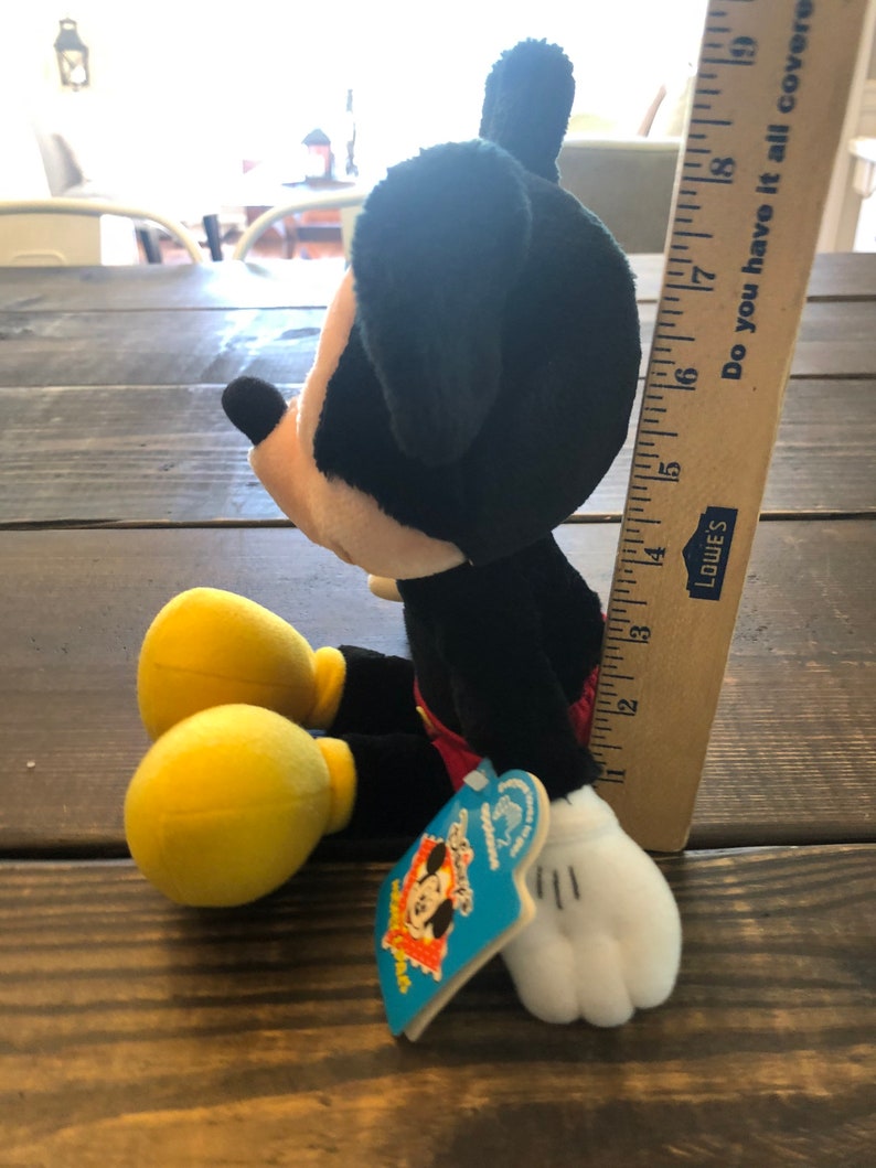 May include: A black and red plush Mickey Mouse toy with yellow shoes and a white tag that says "Disney's Mickey Mouse Clubhouse".