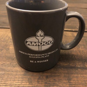 May include: Gray ceramic coffee mug with the Amoco logo and the text "Amoco Performance Products Augusta Plant Be A Winner".
