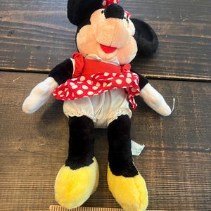 May include: A plush Minnie Mouse toy wearing a red and white polka dot dress with a white petticoat and yellow shoes. The toy is approximately 12 inches tall.