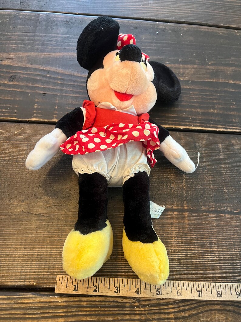 May include: A plush Minnie Mouse toy wearing a red and white polka dot dress with a white petticoat and yellow shoes. The toy is approximately 12 inches tall.