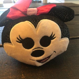May include: A black and white plush toy with a pink bow. The toy has a sparkly black fabric and a white face with embroidered features.