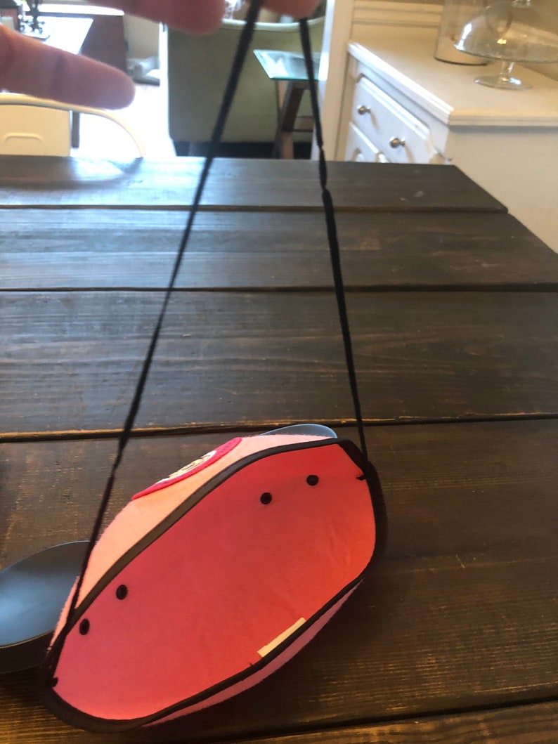 May include: A pink felt Mickey Mouse hat with black trim and a black strap. The hat has a red circle with a white design on the front.