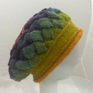 May include: A colorful knitted beret with a braided pattern and a yellow trim. The beret is made of a soft, textured yarn and has a rainbow color gradient.