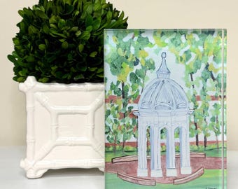 May include: A white glass paperweight with a painting of a white gazebo with a domed roof surrounded by green trees. The text "J. Prange" is in the bottom right corner of the image.