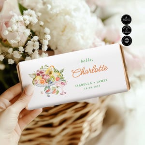 May include: A white chocolate bar wrapper with a watercolor illustration of fruit and a cocktail glass. The text reads "hello, Charlotte" in a script font, with the names Isabella + James and the date 18.08.2035.