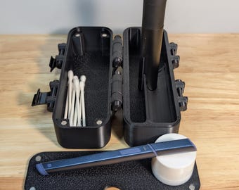 Op de afbeelding: Een zwarte, open, scharnierende koffer met diverse items. Binnenin zitten wattenstaafjes en een cilindrisch voorwerp. Een dienblad bevat een penachtig voorwerp en een kleine witte container. Op een houten oppervlak.