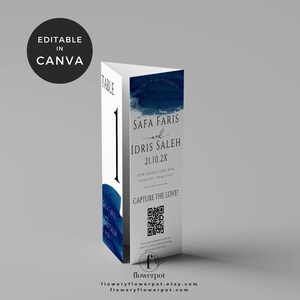 May include: A blue and white wedding table number card with a watercolor design. The card features the names "Safa Faris" and "Idris Saleh" and the date "21.10.2X". It also includes a QR code with the text "Capture the Love!" and the website "floweryflowerpot.com".
