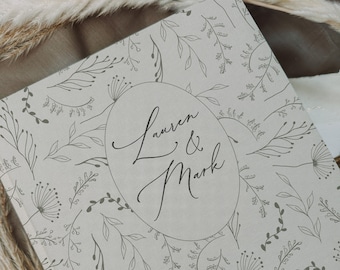 Puede incluir: Un libro de visitas de boda gris claro con un patrón floral y el texto "Lauren & Mark" en un círculo.