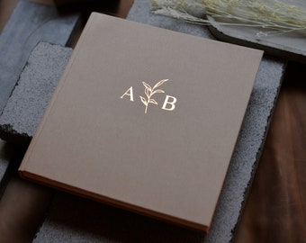 Puede incluir: Un diario de cuero marrón con letras doradas que dicen "A & B" y un pequeño diseño de hoja dorada.
