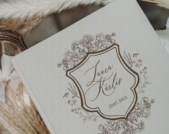 Puede incluir: Un libro de visitas de boda de lino beige con un diseño floral marrón y un escudo con el texto "Laura Karlis" y la fecha "29.07.2024".