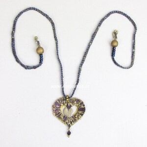 May include: A gray and gold heart-shaped pendant necklace with a woven design. The necklace has two wooden beads and blue beads.