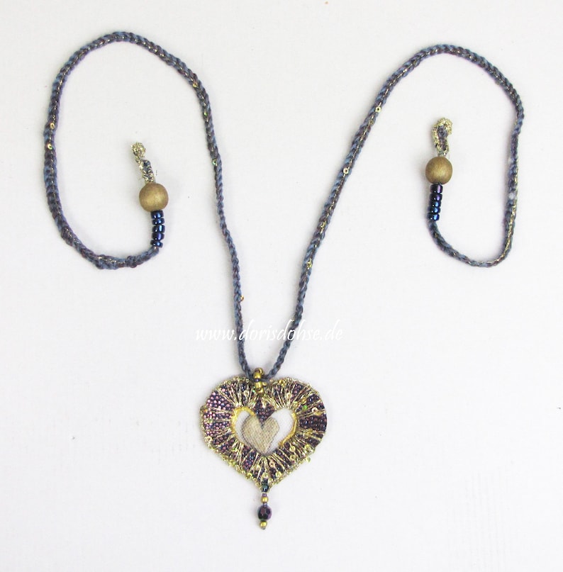 May include: A gray and gold heart-shaped pendant necklace with a woven design. The necklace has two wooden beads and blue beads.