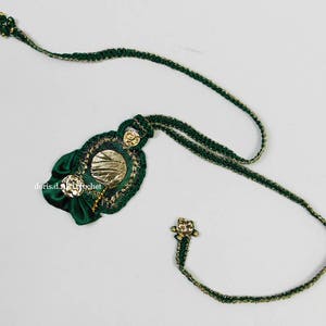 May include: A green and gold crocheted necklace with a decorative pendant featuring a gold circle and green fabric flowers.