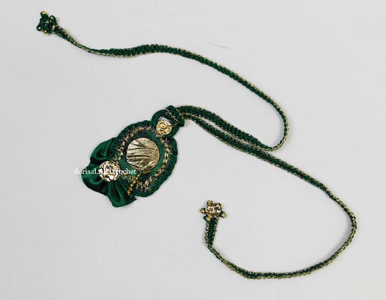May include: A green and gold crocheted necklace with a decorative pendant featuring a gold circle and green fabric flowers.