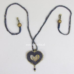 May include: A blue and gold necklace with a heart-shaped pendant. The pendant is made of denim and has a gold heart cut out of it. The necklace is accented with wooden beads and small blue beads.