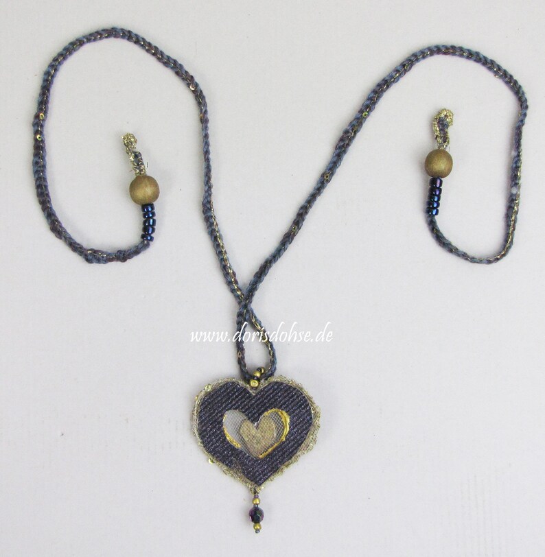 May include: A blue and gold necklace with a heart-shaped pendant. The pendant is made of denim and has a gold heart cut out of it. The necklace is accented with wooden beads and small blue beads.