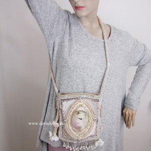 Puede incluir: Un bolso de mano de ganchillo con flecos de cuentas y un diseño floral. El bolso tiene una pequeña ventana ovalada con un retrato pintado en su interior. El texto "www.dorisdohse.de" es visible en el bolso.