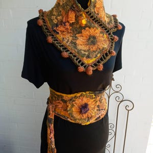 May include: A yellow, green, and brown crocheted neck warmer with a floral design and a large button. The neck warmer is worn on a black dress with a matching yellow, green, and brown belt.