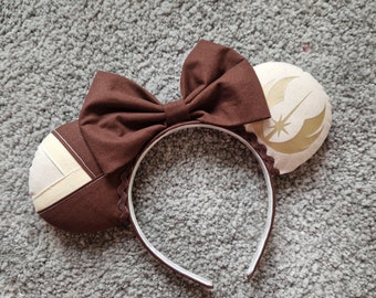 May include: Brown fabric headband with a white and gold fabric bow and a white fabric ear with a gold star wars symbol.