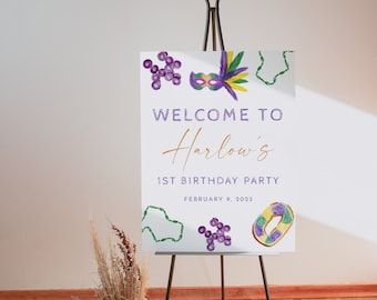 Könnte beinhalten: Willkommen zur 1. Geburtstagsparty von Harlow mit einem violetten, grünen und goldenen Mardi Gras-Thema. Das Schild zeigt eine violette und grüne Maske, Perlen und einen Donut.