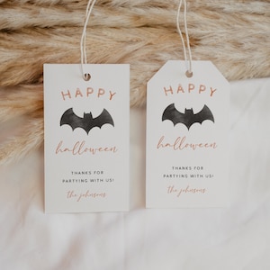 Peut inclure: Deux &eacute;tiquettes cadeaux blanches avec des chauves-souris noires et le texte "Happy Halloween" en police de caract&egrave;res cuivr&eacute;e. Le texte "Merci d'avoir fait la f&ecirc;te avec nous !" et "the johnsons" sont &eacute;galement en police de caract&egrave;res cuivr&eacute;e.