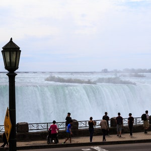 May include: A view of Niagara Falls from a viewing platform with a black street lamp and a group of people looking out at the falls.