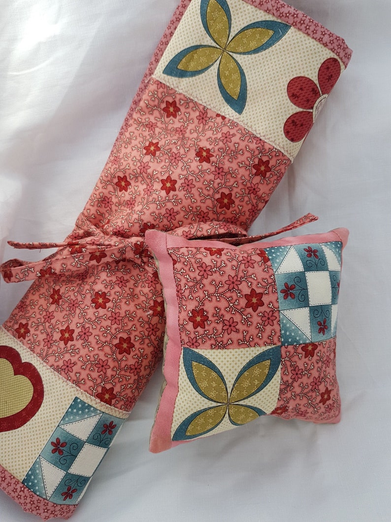 May include: Two pink and white patchwork fabric pillows with floral and geometric patterns. The larger pillow is a long rectangular shape and the smaller pillow is square.